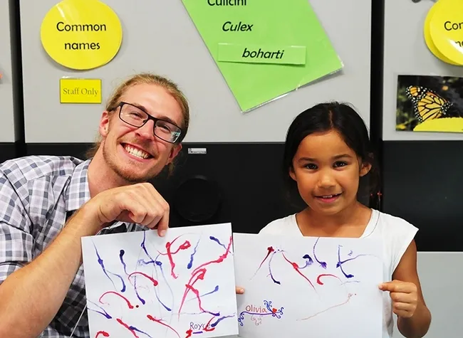 NAFEA member Royce Cumming of Salinas Valley and 6-year-old Olivia Storms of Davis show their maggot art paintings. (Photo by Kathy Keatley Garvey)