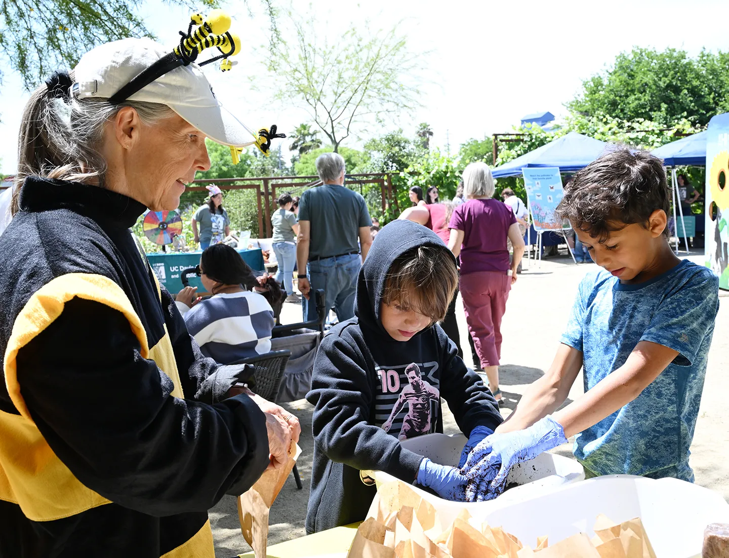 Bettina the Bee (Wendy Mather) showing two boys how to make seed cakes. (Photo by Kathy Keatley Garvey)