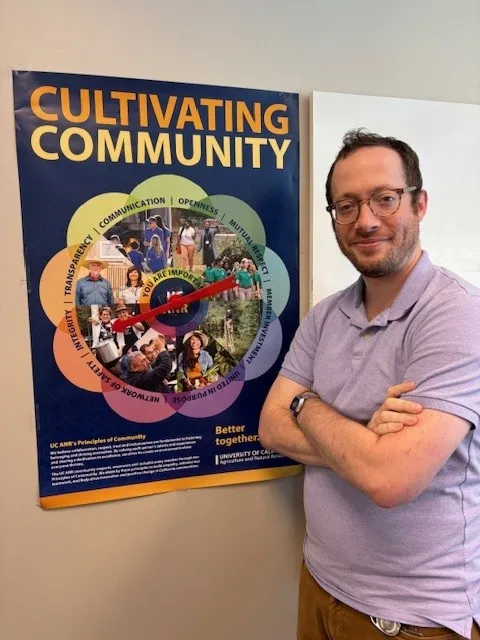 Scott Leaf standing in front of the Principles of Community Poster with a spinner attached