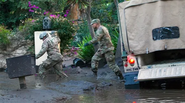 Sgts. Paiz and Espinoza of the California National Guard trudge through knee-deep mud to rescue three people and a dog trapped inside their Montecito home. Air National Guard photo by Senior Airman Crystal Housman.