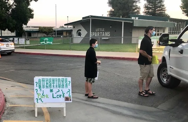 Youth and adult with face masks approach a car.