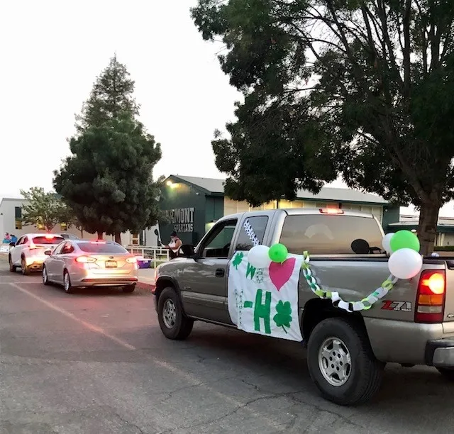 Cars and truck lined up. Truck is decorated with 4-H banner and balloons