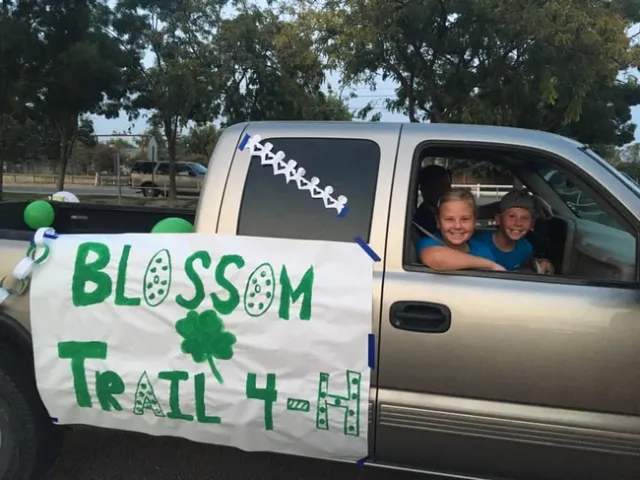 Truck decorated with Blossom Trail 4-H banner with 2 youth looking out window.