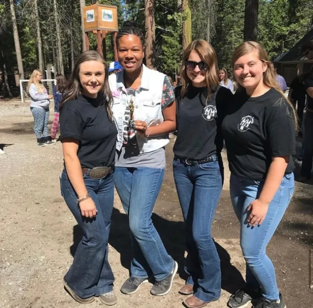 3 youth in black shirts pose with youth in white vest holding an award