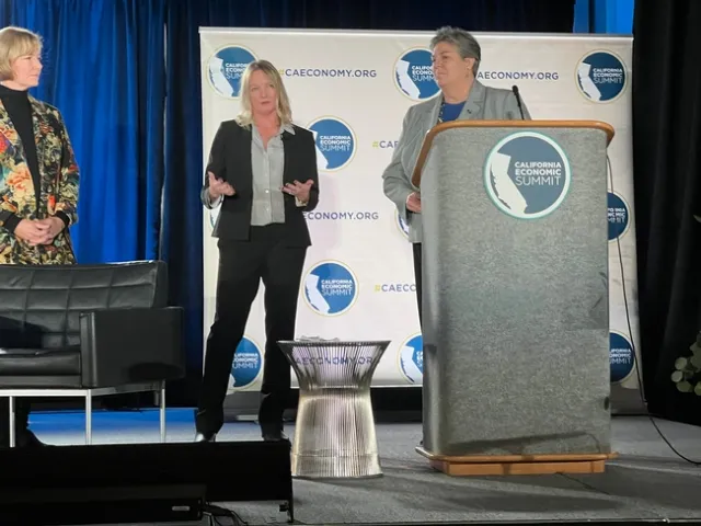 Three women dressed in suits stand on stage.