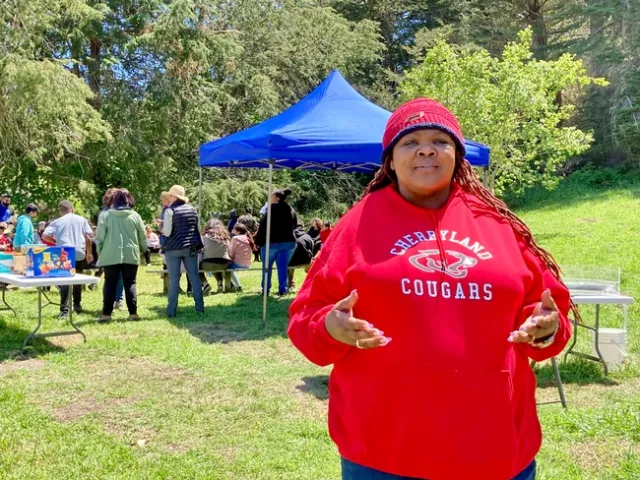 Campbell, wearing a red Cherryland Cougars sweatshirt, speaks as children gather in the background.