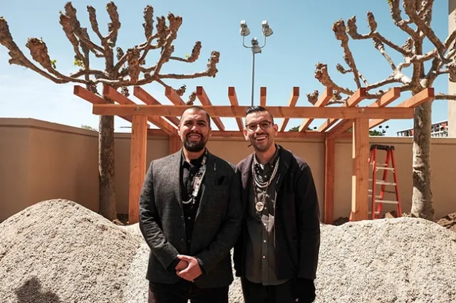 Two men in dark suits pose together outdoors.