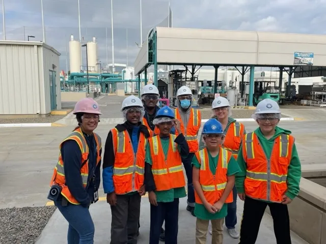 A group of young students posing in front of a water recycling facility with their tour guide.