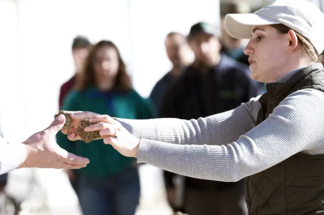 Woman hands two soil clods to a disembodied hand.