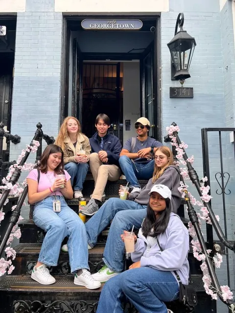 Six youth holding disposable drink cups sitting on steps in front of building entrance