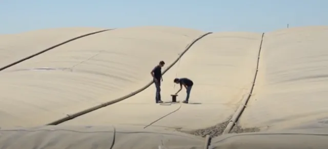 Pramod Pandey and another guy stand what looks like a humongous inflated pillow stretching over the top of a dairy lagoon.
