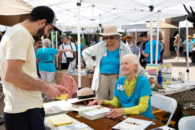 A woman is sitting down at a table, talking to a young man who is standing on the other side of the table.