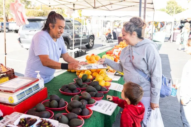 Woman shows children cucumbers at a farmers market in Santee, California