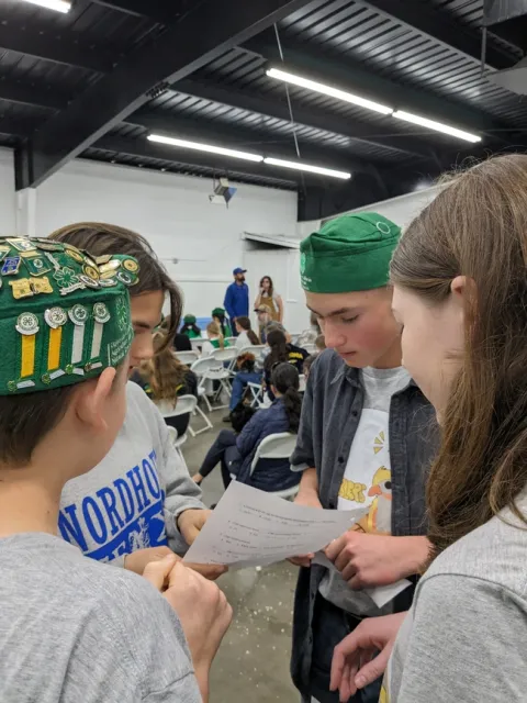 In a large room, 4 youth stand in a circle looking at a paper.
