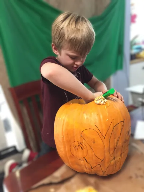 blonde boy carving out a pumpkin