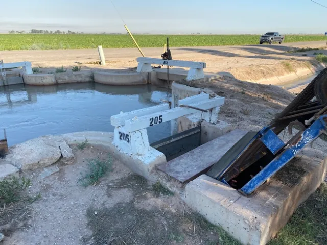 Water pump and small pool of water next to a crop field