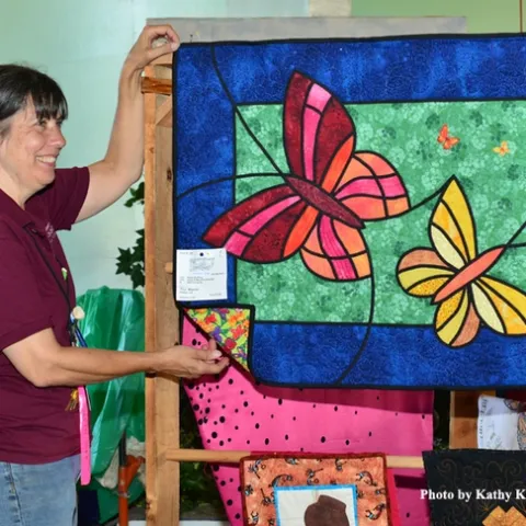 McCormack Hall superintendent Gloria Gonzalez hangs "Butterfly Lovers" by Tina Waycie of Vallejo. (Photo by Kathy Keatley Garvey)