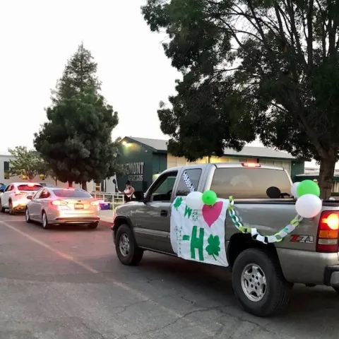 Cars and truck lined up. Truck is decorated with 4-H banner and balloons