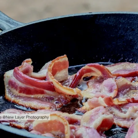 Bacon frying in a black iron skillet.