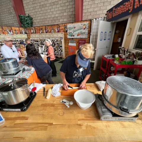 Farm-house themed booth with two volunteers speaking to visitors and third volunteer cutting vegetables.