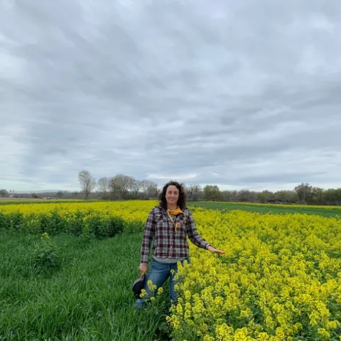 Sarah stands between a green field and yellow flowering mustard.