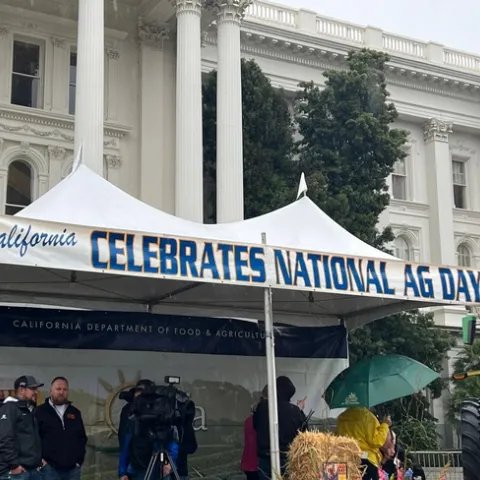 White popup canopy with the words: "CALIFORNIA CELEBRATES NATIONAL AG DAY" in front of State Capitol building.