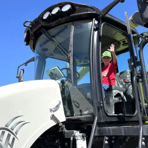 A boy sits in the cab of a harvester