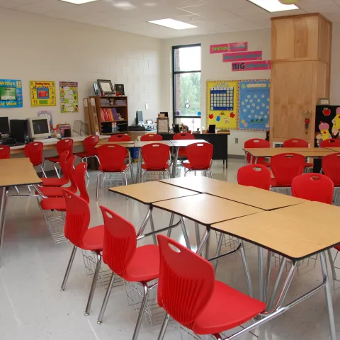 a classroom with red chairs, a table and posters on the walls