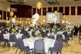 Auditorium decorated for the centennial celebration. Rounds tables with white table clothes and yellow and white balloons scattered throughout the roo