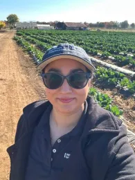 Preet Ahluwalia, wearing sunglasses, stands in a field at a farm