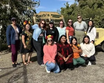 A group of people smile as they stand in front of a produce stand sign