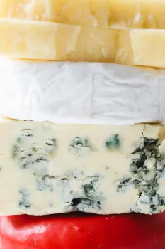 Various cheeses stacked on top of one another with various colors: light yellow, white, marbled with green, and red wax.