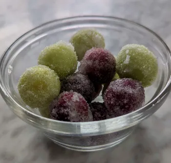 A small bowl full of frozen grapes coated in citric acid and sugar.