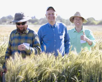 hree people standing in an open field at an Agricultural Experiment Station (AES), smiling and facing the camera