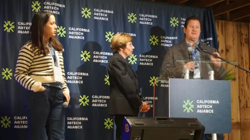 Gabe Youtsey speaks at a podium while Karen Aceves and Karen Ross look on at AgTech Alliance press conference