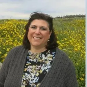 A woman with dark brown hair standing in a field of yellow flowers
