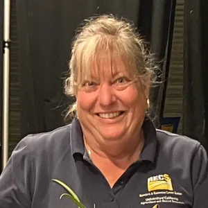 A woman with light hair and bangs wearing a blue polo with a UC ANR REC System Logo